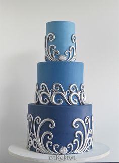 a three tiered blue and white cake with swirls on it's sides