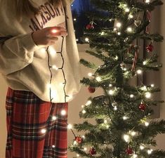 a girl standing next to a christmas tree holding a cell phone in her hand and looking at it