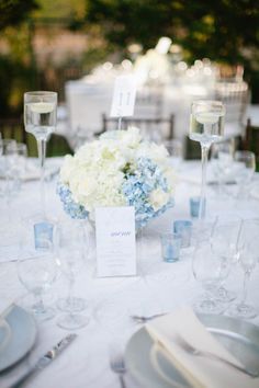 the table is set with white and blue flowers, silverware, and wine glasses