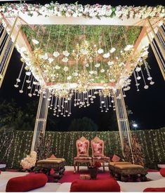 an outdoor wedding setup with chandeliers and flowers hanging from the ceiling, surrounded by red velvet chairs