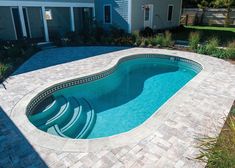 an empty swimming pool in the middle of a backyard with brick pavers around it