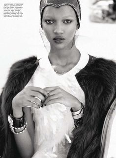 a black and white photo of a woman in a fur coat with rings on her finger