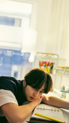 a young boy laying on top of a desk next to a laptop computer and yellow pencils