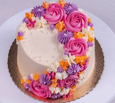 a white cake with pink, purple and orange flowers on the top is sitting on a gold platter