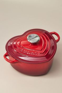 a red casserole dish with a lid and handle sitting on a white surface