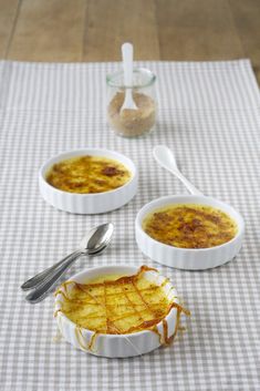 two bowls filled with food sitting on top of a checkered table cloth next to spoons