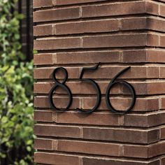 a brick building with a metal number sign on it's side and trees in the background