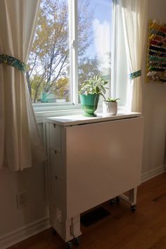 a white cabinet sitting in front of a window next to a potted plant on top of it