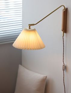 a lamp that is on the wall next to a pillow and window with blinds behind it