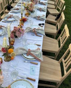 a long table is set with plates and candles for an outdoor dinner party in the grass