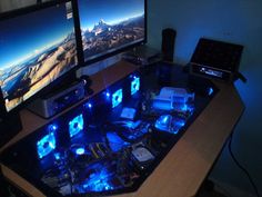 two computer monitors sitting next to each other on a desk with blue lights in front of them