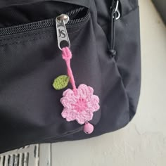 a pink crocheted flower is attached to a black backpack with a metal hook