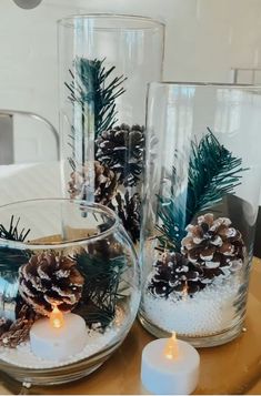 three clear glass vases with pine cones and candles on a table in a living room