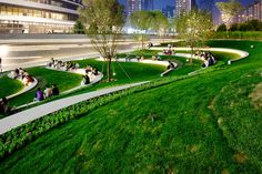 people are sitting on the grass in front of a large building at night with tall buildings behind them