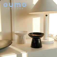 two lamps and a bowl sit on a white table in front of a window with the words oumo pet shop