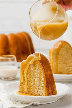 someone is pouring orange juice into a bundt cake on a white plate with another bundt cake in the background