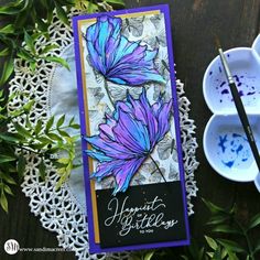 a card with purple flowers on it next to two bowls and paintbrushes sitting on a doily