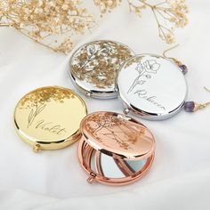 three compact mirrors with writing on them sitting on a white surface next to dried flowers