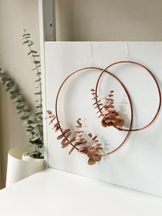 two metal hoops with flowers and leaves hanging on the wall next to a plant