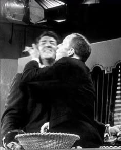 black and white photograph of two men sitting at a table, one kissing the other