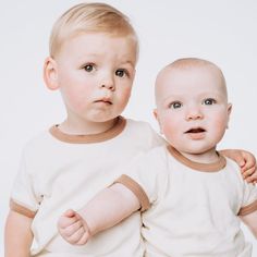 two toddlers standing next to each other in front of a white background with one looking at the camera