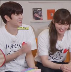 two young people sitting next to each other holding tennis racquets