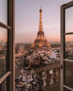 the eiffel tower is lit up at night from an open window with flowers