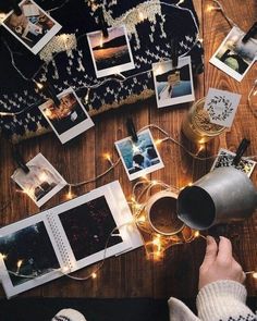 a person holding a coffee mug in front of pictures on a table with string lights