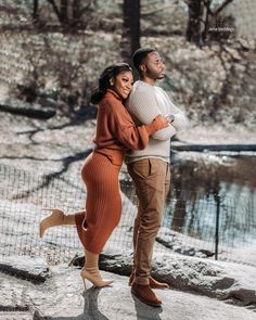 a man and woman standing next to each other in front of a lake with snow on the ground