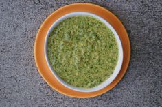 a yellow and white bowl filled with green soup on top of a gray countertop