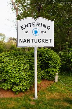 a white street sign sitting on the side of a lush green field