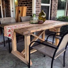 a wooden table sitting on top of a patio next to a chair and vase filled with flowers