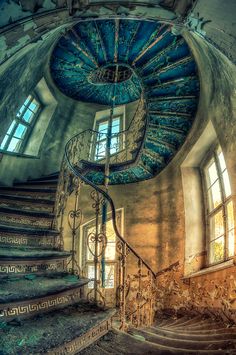 a spiral staircase in an old building with blue paint on the walls and windows above it