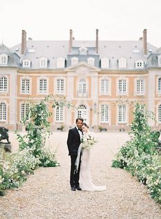 a bride and groom standing in front of a large building with lots of greenery