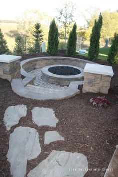 a stone fire pit surrounded by trees and shrubs