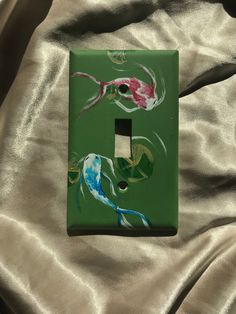 a green light switch cover with two fish painted on it