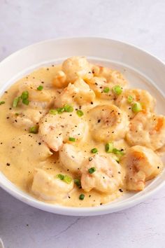 a white bowl filled with shrimp and dumplings covered in gravy on top of a table