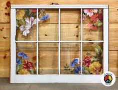 an old window with flowers painted on the glass and some wood behind it, in front of a wooden wall