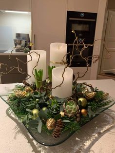 candles and greenery in a glass bowl on a kitchen counter top with pine cones