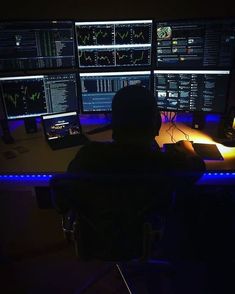 a man sitting at a desk in front of three computer monitors with multiple screens on it