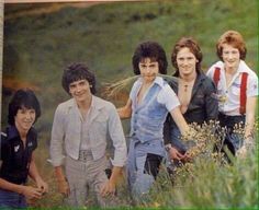 a group of young people standing next to each other in a field with tall grass