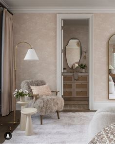 the bedroom is decorated in neutral colors and features a fur - lined chair, side table, mirror, and stool