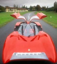 a red sports car parked on the side of a road next to a lush green field