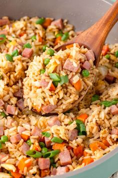 a pan filled with rice, ham and green onions being stirred by a wooden spoon