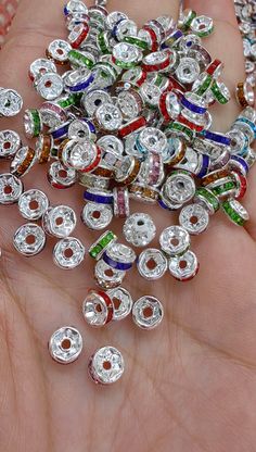 a person's hand holding several different colored and silver jewelry pieces in their palm