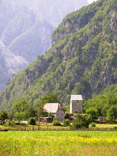 an old farm house sits in the middle of a field with mountains in the background