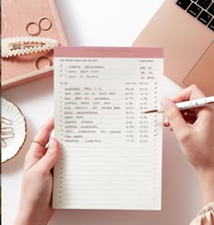 a person writing on a piece of paper next to a laptop and other office supplies