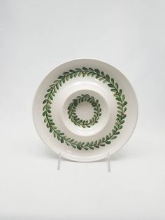 a white bowl with green leaves on it and a spiral design in the center, sitting on a stand