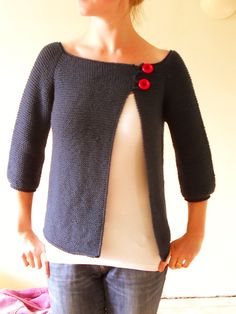 a woman standing in front of a white wall wearing a black sweater with red buttons