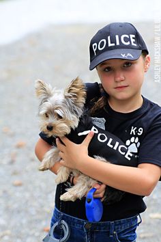 a young boy holding a small dog wearing a police t - shirt and baseball cap